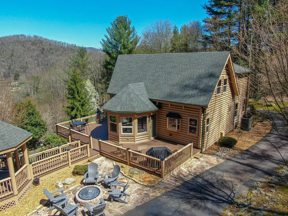 A spacious wooden deck with a cozy fire pit, surrounded by tall trees and offering unobstructed mountain views. The scene evokes relaxation and camaraderie, with plenty of space for gatherings or quiet moments.
