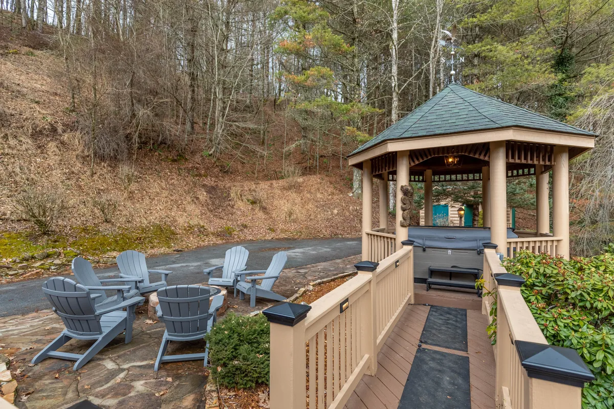A tranquil outdoor space featuring a gazebo with comfortable seating and a gently winding pathway set in natural surroundings. The area looks perfect for gathering, socializing, or quietly enjoying the views, with hints of a fire pit area that reinforces its use in all seasons.