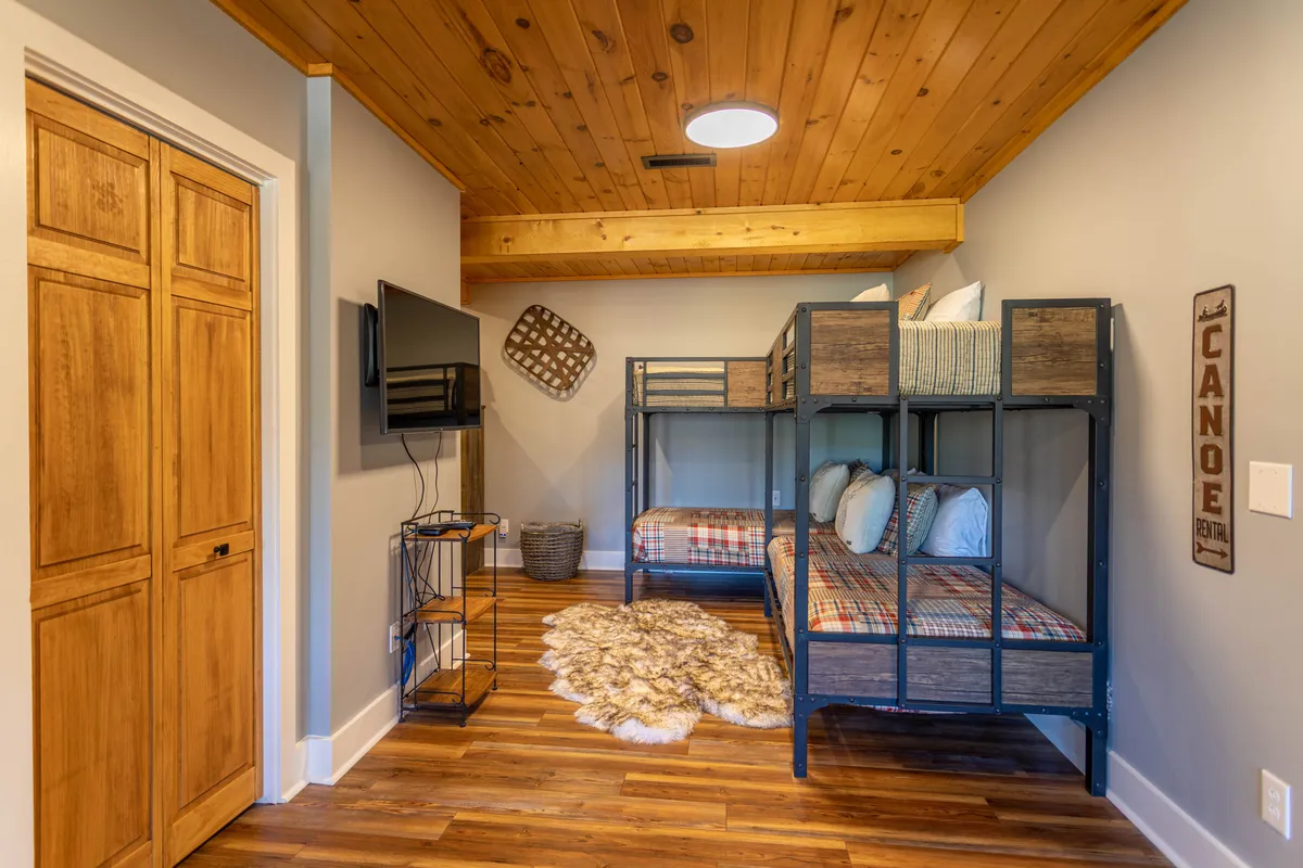 A bunkroom with built-in bunk beds, a TV, wooden door, decorative basket, and playful décor, including a 'cabin' sign. The space is perfect for children or teens to enjoy movie nights or sleepovers.
