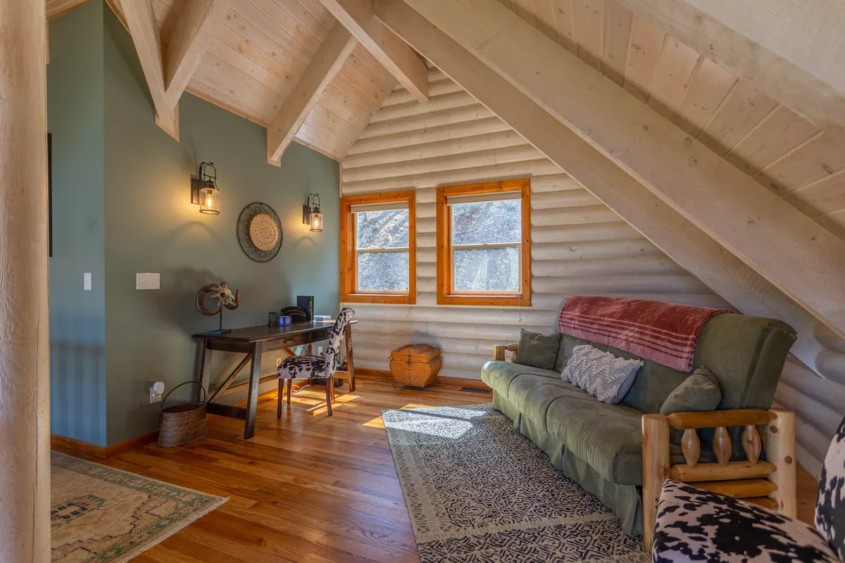 A lofted space featuring a comfortable sofa, a desk positioned near windows, and decorative touches. The area is bathed in natural light, making it ideal for remote work or creative pursuits with inspiring views.